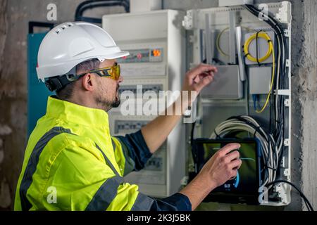 Man an electrical technician working in a switchboard with fuses, uses a tablet. Stock Photo