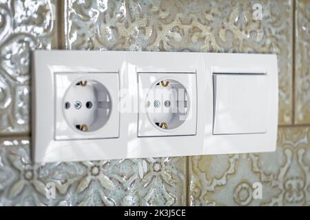 White plastic walk-through switches and sockets on a white wall. Stock Photo