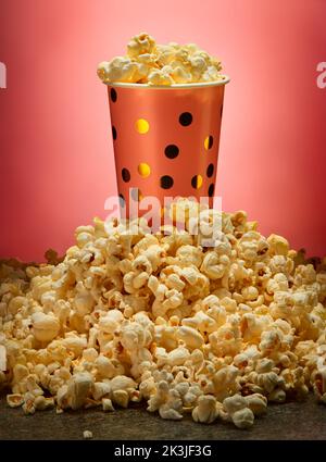 Full pink paper cup with gold dots in big popcorn pile on marble countertop and pink background Stock Photo