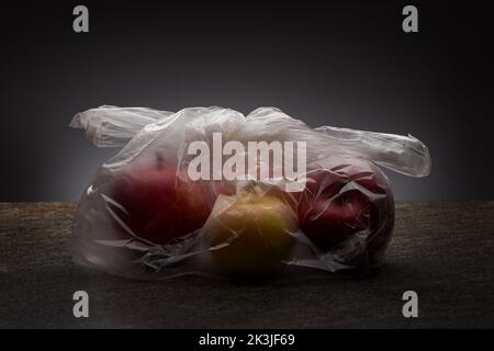 Organic red and yellow apples in transparent plastic bag on marble countertop and grey background Stock Photo