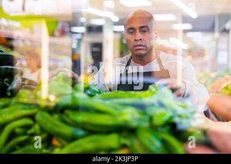 Supermarket worker in black apron cheking vegetables Stock Photo