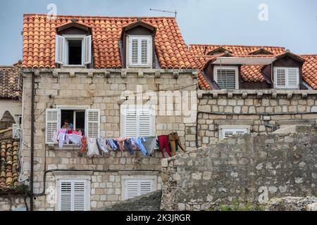 Woman hanging the laundry on a washing line outside a window with white shutters.Old town of Dubrovnik, Croatia Stock Photo