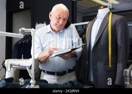 Professional tailor communicates with the client on mobile phone and takes notes in notebook Stock Photo
