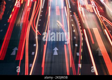 Light trails of cars on urban road during evening traffic jam. Illuminated arrows of road marking. Stock Photo