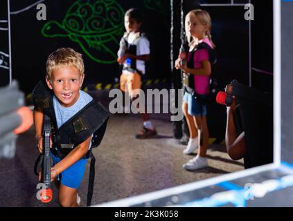 Excited little boy aiming laser gun at other players during lasertag game in dark room Stock Photo