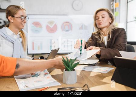 Focused african and caucasian women having paperwork at office. Female managers with gadgets in desk analysing financial report. People, business and technology concept. Stock Photo