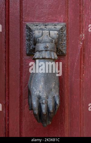 Closeup view of textured vintage brass door knocker in shape of hand isolated on old dark red wooden door, Montpellier, France Stock Photo