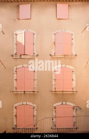 Many wooden pink shutters on pastel orange color painted wall building. European style closed windows with ornamental frame on building facade Stock Photo