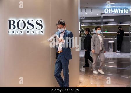 A man wearing a suit is seen reading outside the German clothing brand Hugo Boss store in Hong Kong. Stock Photo