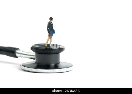 Miniature people toy figure photography. Medical checkup schedule concept. A businesswoman standing above stethoscope. Isolated on white background. I Stock Photo