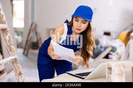 Female contractor in blue uniform using laptop at construction site Stock Photo