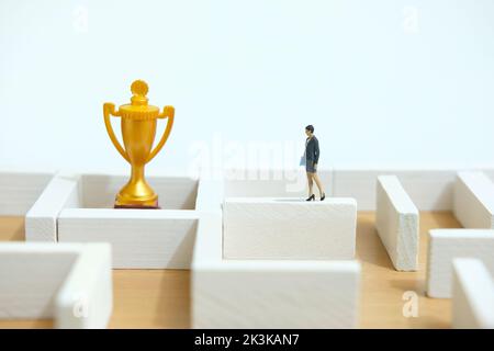 Miniature people toy figure photography. Business solution concept. A businesswoman walking above maze labyrinth wall looking for golden trophy, solut Stock Photo