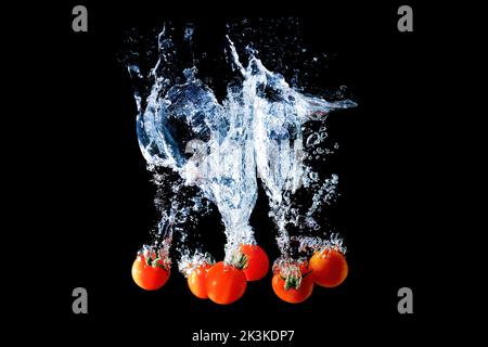 Cherry tomatoes dropped in water with splashes and bubbles isolated on black background. Stock Photo