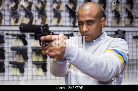 Focused latin american man aiming with pistol in gun shop Stock Photo