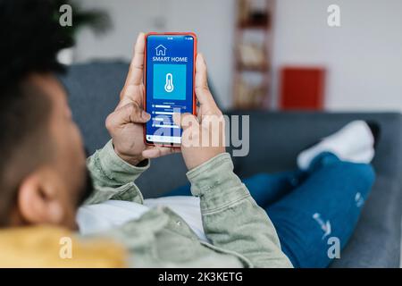 Young adult man using IOT app on smart phone controlling temperature at home Stock Photo