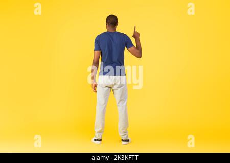 Back View Of Black Guy Pointing Finger Upward, Yellow Background Stock Photo