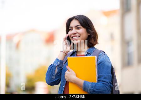 Happy Middle Eastern Student Female Talking On Cellphone While Walking Outdoors Stock Photo