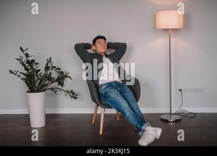 Satisfied happy mature chinese man relaxing with closed eyes, enjoy peace and quiet, sit in armchair Stock Photo