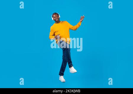 Positive black man listening to music and dancing, using headphones Stock Photo