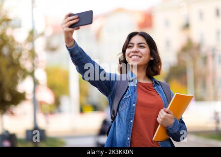 Cheerful Arab Female Student Taking Selfie With Smartphone Outdoors Stock Photo