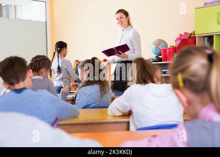 Positive female teacher standing at blackboard with schoolgirl during lesson in classroom Stock Photo