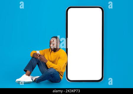 Happy black man sitting on floor, using smartphone Stock Photo
