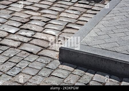 The corner of the sidewalk made of stone tiles with access to the road paved with cobblestones close-up of a clean old road on a sunny day cityscape, Stock Photo