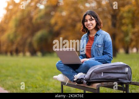 Remote Work. Smiling Young Arab Woman Sitting With Laptop On Bench Outdoors Stock Photo