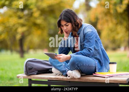 Tired Arab Student Woman Using Digital Tablet While Sitting On Bench Outdoors Stock Photo