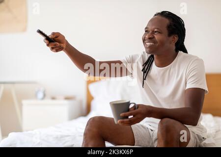 Smiling Black Man Drinking Coffee And Watching TV While Relaxing At Home Stock Photo