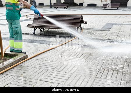 Sweeper cleaning a public park with water using a hosepipe. Public maintenance concept. Copy space Stock Photo