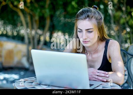 Portrait of a young caucasian woman posing outdoor in a garden with a laptop looking for information in internet. Lifestyle concept. Stock Photo