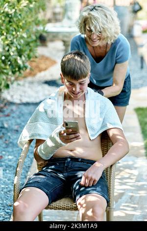 Portrait of a mother cutting young caucasian boy's hair outside in a garden. Lifestyle concept. Stock Photo