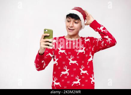 A surprised caucasian young man wearing christmas clothes on a white background holding a smart phone Stock Photo