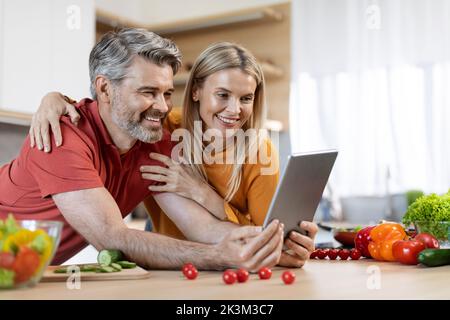 Happy spouses using digital tablet while cooking Stock Photo