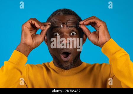 Amazed african american man removing eyeglasses on blue Stock Photo