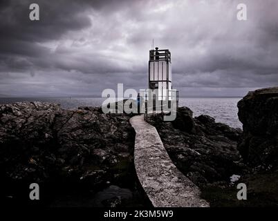 A female walker on the lighthouse concrete path between folded rocks at the Point of Sleat, Sleat, Isle of Skye, Scotland. Stock Photo