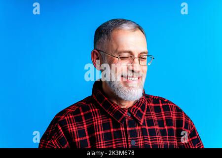 Close-up portrait of intelligent shy man looking down in blue studio background Stock Photo