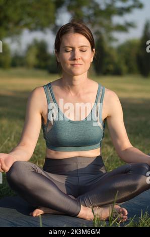 Beautiful young woman meditates in the park at sunset. Woman practices yoga in the park. Yoga in nature Stock Photo
