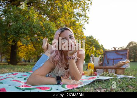 Young vegetarian smiling woman lying on picnic mat ready to start picinc. Stock Photo
