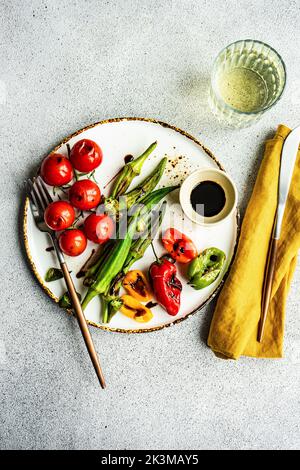 Healthy dinner with bbq bamia, paprika peppers and cherry tomatoes with soy and balzamico sauces served with glass of cold dry wine Stock Photo