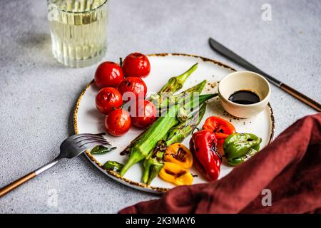 Healthy dinner with bbq bamia, paprika peppers and cherry tomatoes with soy and balzamico sauces served with glass of cold dry wine Stock Photo