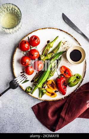 Healthy dinner with bbq bamia, paprika peppers and cherry tomatoes with soy and balzamico sauces served with glass of cold dry wine Stock Photo