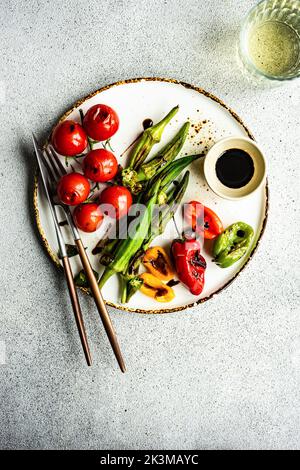 Healthy dinner with bbq bamia, paprika peppers and cherry tomatoes with soy and balzamico sauces served with glass of cold dry wine Stock Photo