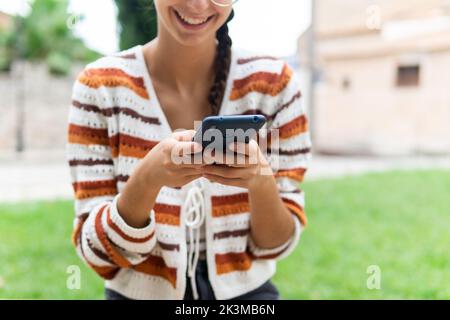 Positive young female messaging on social media via mobile phone while looking at screen Stock Photo