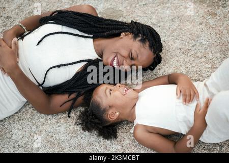 Top view of happy black mom and daughter in white clothes smiling and looking at each other while lying on stone surface together Stock Photo