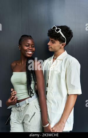 Headshot of young diverse woman and man with curly hair holding hands while looking at each other on gray background Stock Photo