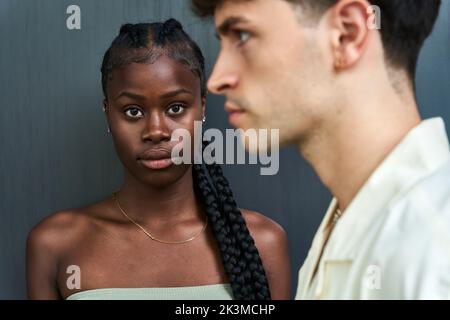 Unemotional African American female model with long braids looking at camera standing close to diverse emotionless guy on gray background Stock Photo