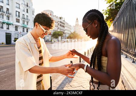 Cheerful black woman in stylish clothes smiling while dancing with boyfriend near road on sunlit city street Stock Photo