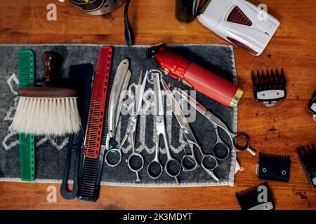 Top view of various barber instruments including scissors trimmers combs razor and brush placed on towel on wooden table in grooming salon Stock Photo